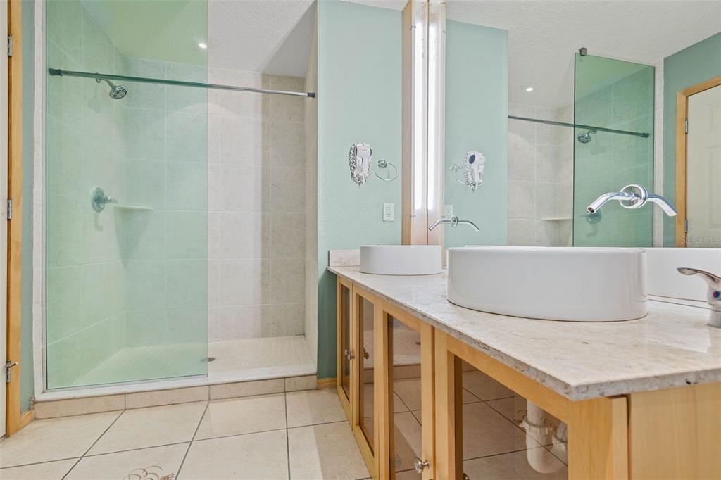 A bathroom features a glass-enclosed shower, two vessel sinks on a stone vanity, and light-colored cabinetry — 101 PALM HARBOR PARKWAY UNIT C231, PALM COAST, FL