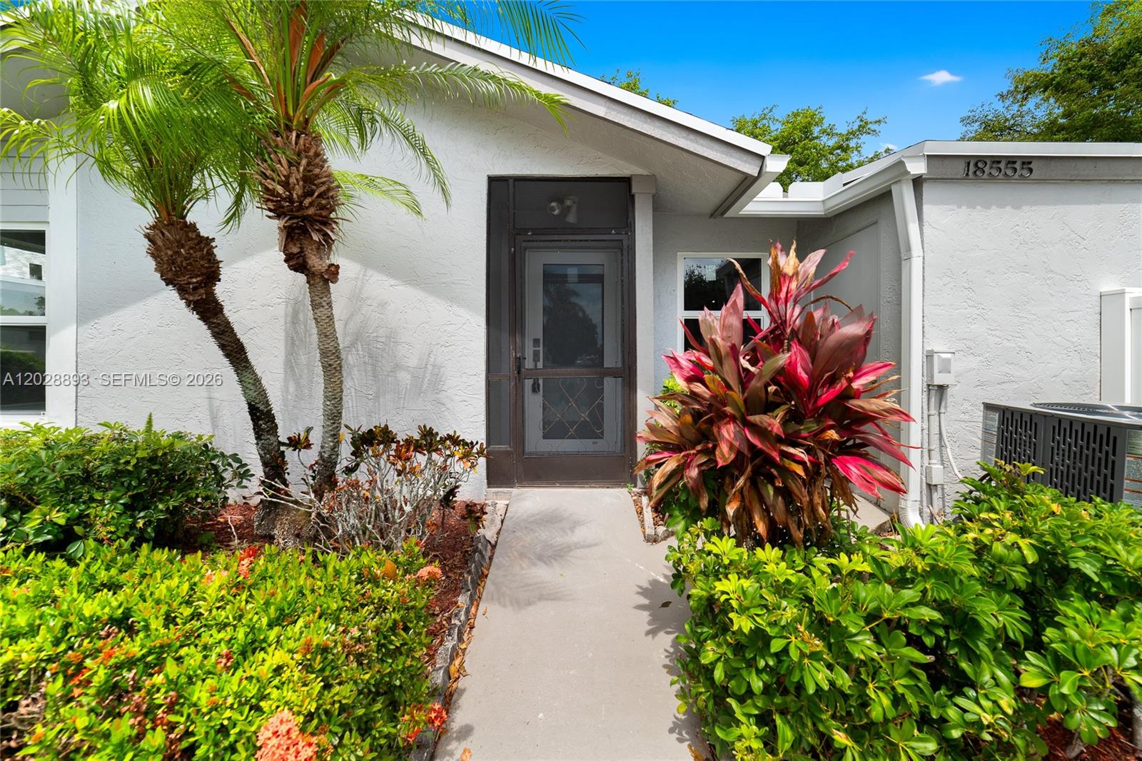 The exterior of a white house features a front door, a walkway, and tropical landscaping — 18555 Egret Way, Boca Raton FL 33496, BOCA RATON, FL