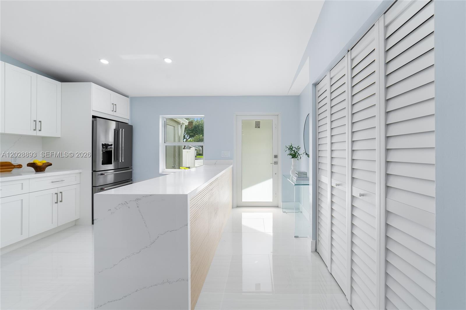 A modern kitchen features white cabinetry, a quartz waterfall island, and white tile flooring — 18555 Egret Way, Boca Raton FL 33496, BOCA RATON, FL