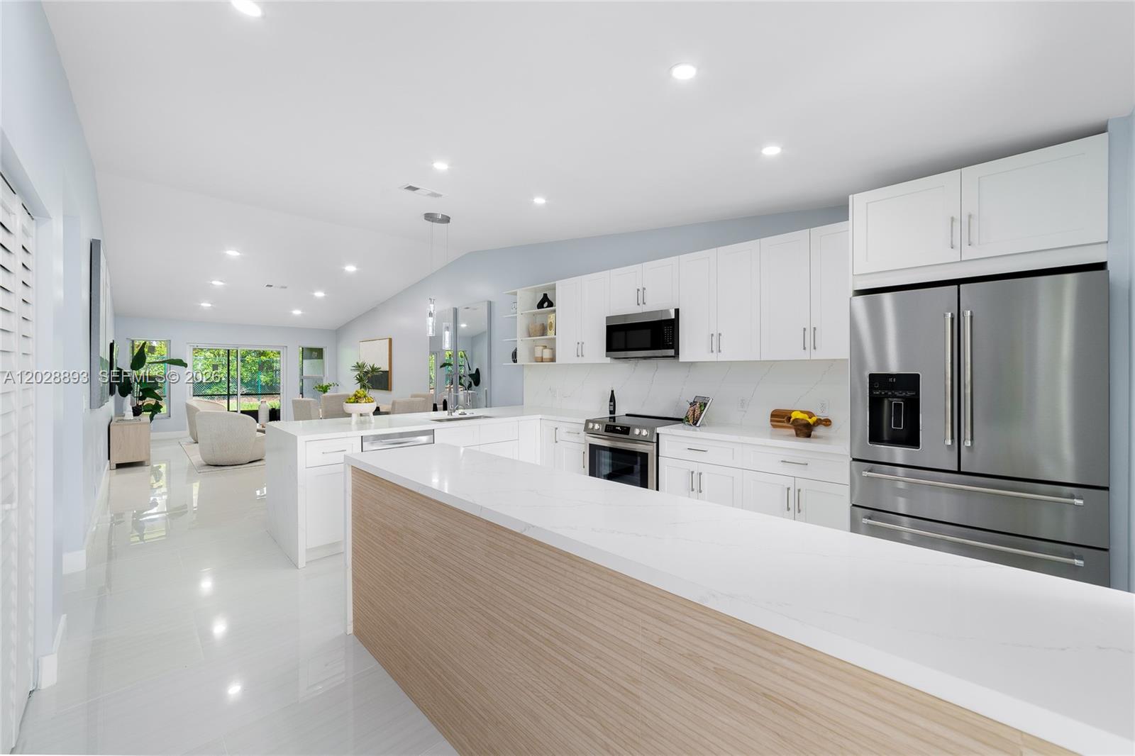 A modern kitchen features white cabinetry, stainless steel appliances, and a wood-paneled peninsula island — 18555 Egret Way, Boca Raton FL 33496, BOCA RATON, FL