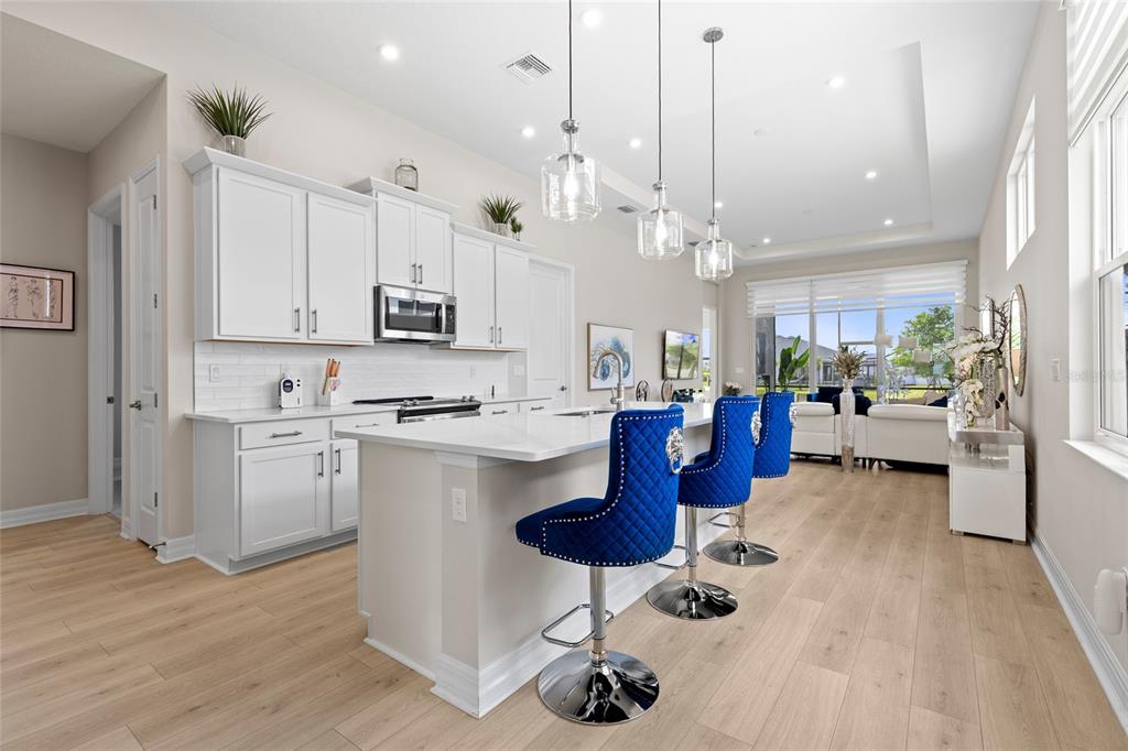 A modern kitchen features white cabinetry, a quartz island with blue stools, and light flooring — 819 LILIANA DRIVE, DELAND, FL