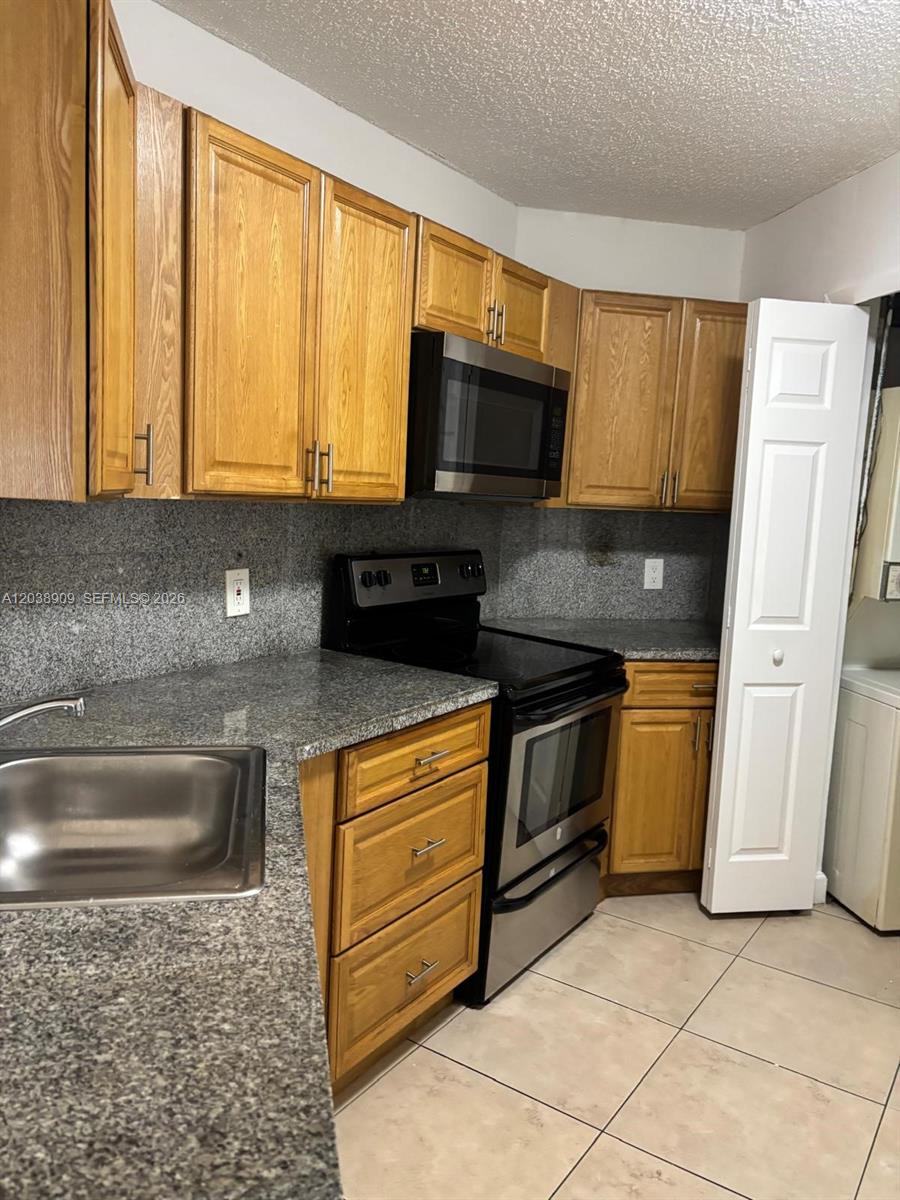 A kitchen features wooden cabinets, granite countertops, stainless steel appliances, and tile flooring — 6276 NW 186th St # 204, Hialeah FL 33015, HIALEAH, FL