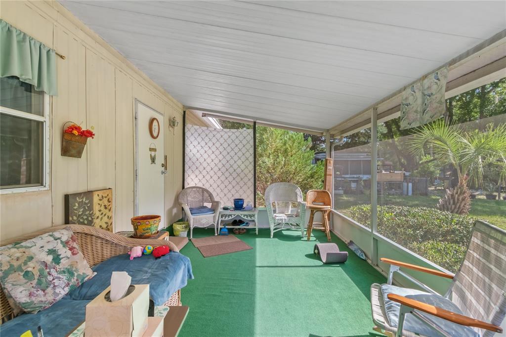 A screened-in porch features green carpet, wicker furniture, and a view of the yard — 5888 SE 164TH AVENUE, OCKLAWAHA, FL