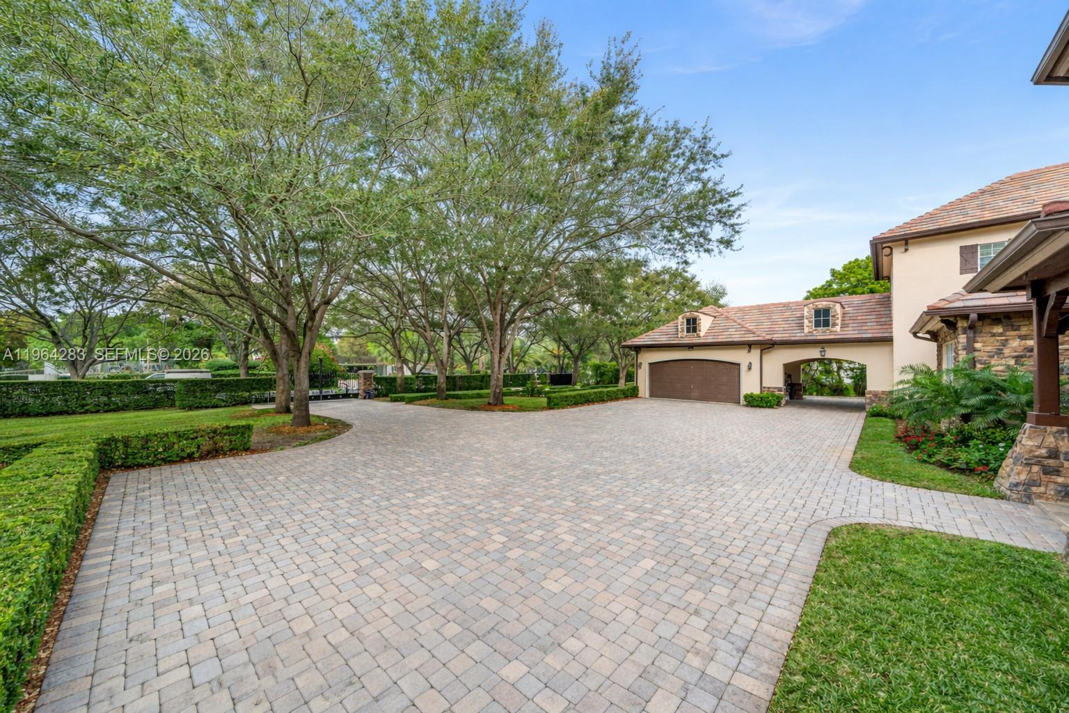 A paved driveway leads to a garage and a stone-accented house under large trees — 12270 SW 45th St, Miami FL 33175, MIAMI, FL