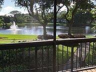 A view of a pond with a fountain from a screened-in balcony with railings — 2025 Lavers Circle # D206, Delray Beach FL 33444, DELRAY BEACH, FL