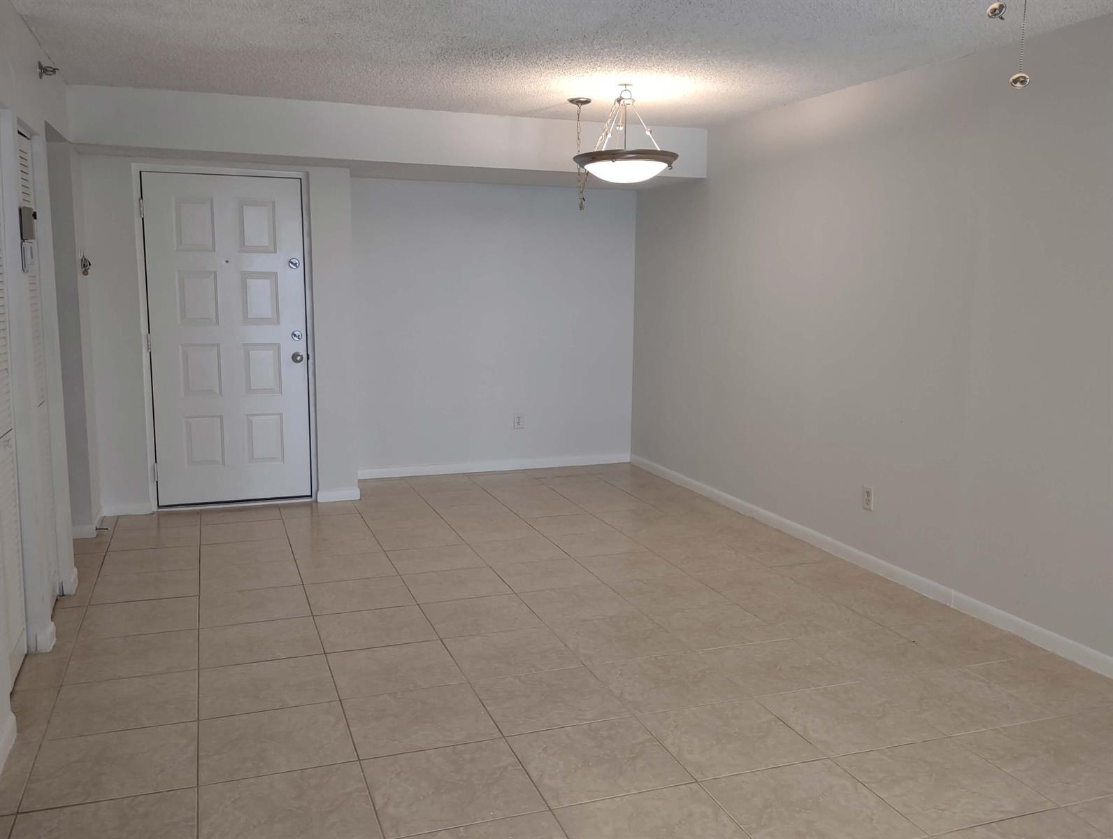 An empty room with light-colored tile flooring, a white front door, and a hanging light fixture — 2025 Lavers Circle # D206, Delray Beach FL 33444, DELRAY BEACH, FL