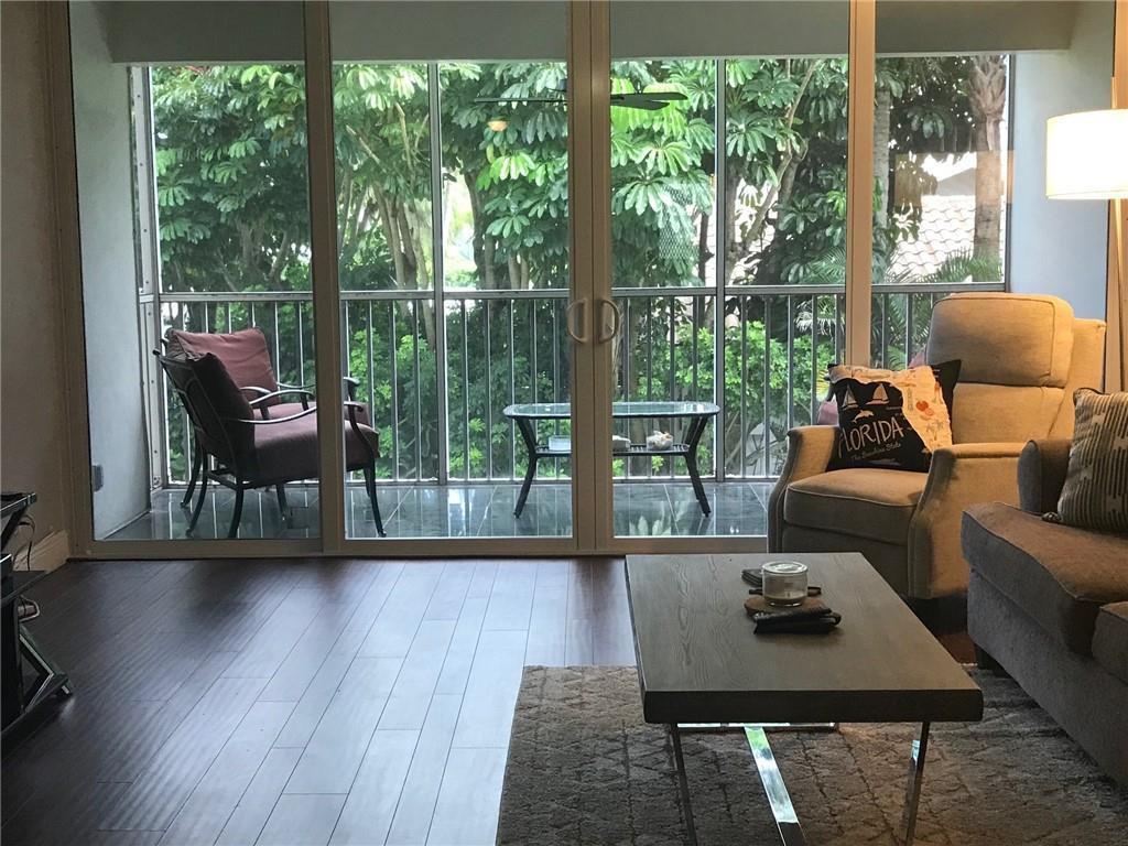 A living room with dark wood floors, a coffee table, and sliding doors to a balcony — 698 NE Spanish River Boulevard # 0250, Boca Raton FL 33431, BOCA RATON, FL