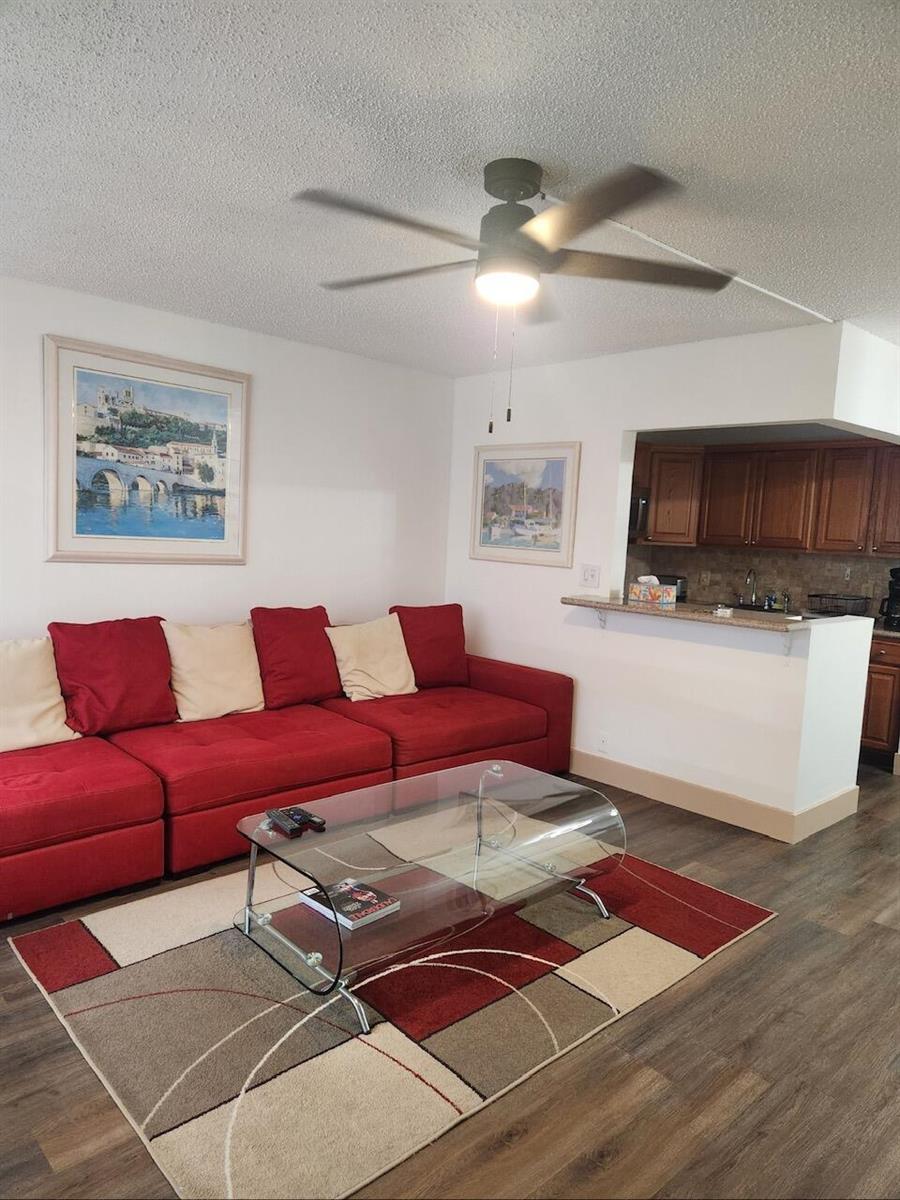 A living room features a red sectional sofa, a glass coffee table, and a ceiling fan — 102 Westbury E # 102, Deerfield Beach FL 33442, DEERFIELD BEACH, FL