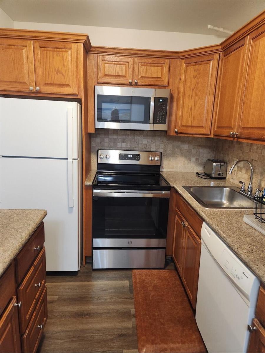 A kitchen features wood cabinets, stainless steel appliances, a white refrigerator, and granite countertops — 102 Westbury E # 102, Deerfield Beach FL 33442, DEERFIELD BEACH, FL