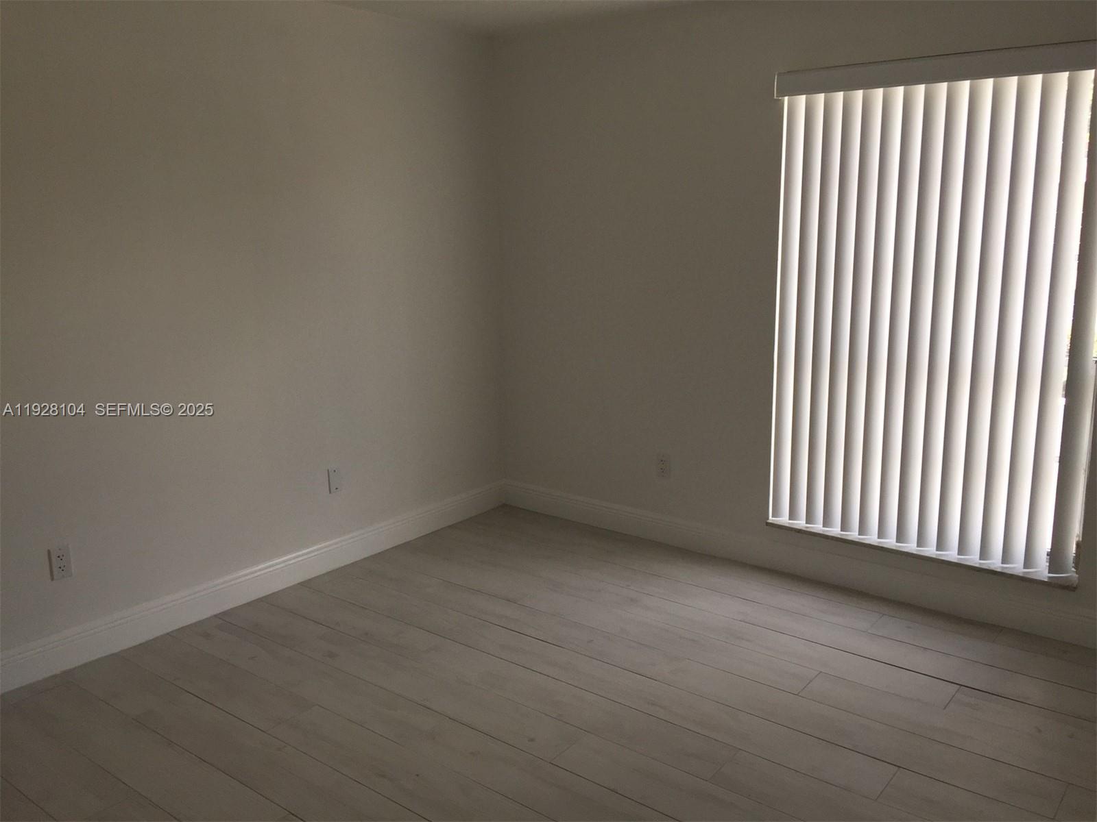 An empty room features light-colored wood-look flooring, plain walls, and vertical window blinds — 10740 N Kendall Dr # 24, Miami FL 33176, MIAMI, FL
