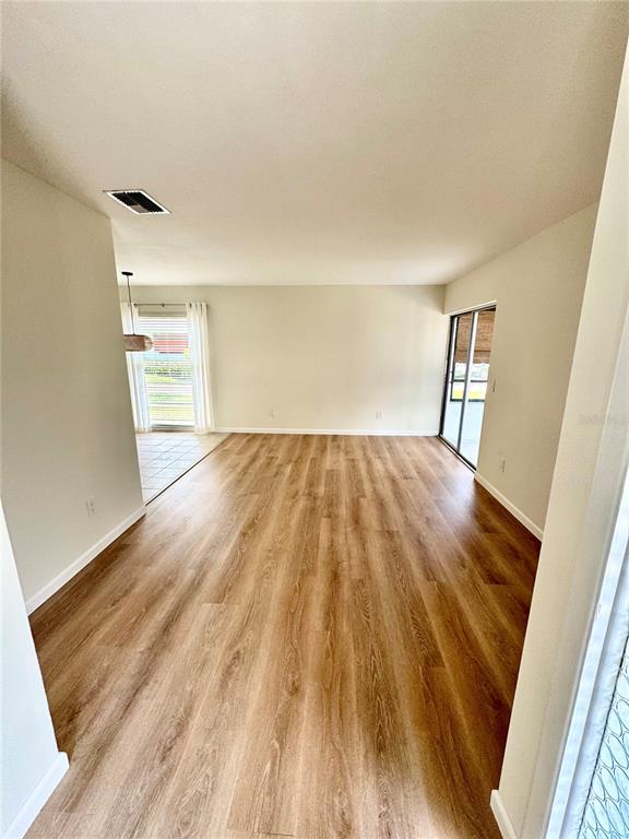 An empty living area features light wood-look flooring, neutral walls, and a sliding glass door — 1610 BERWICK COURT UNIT D, PALM HARBOR, FL
