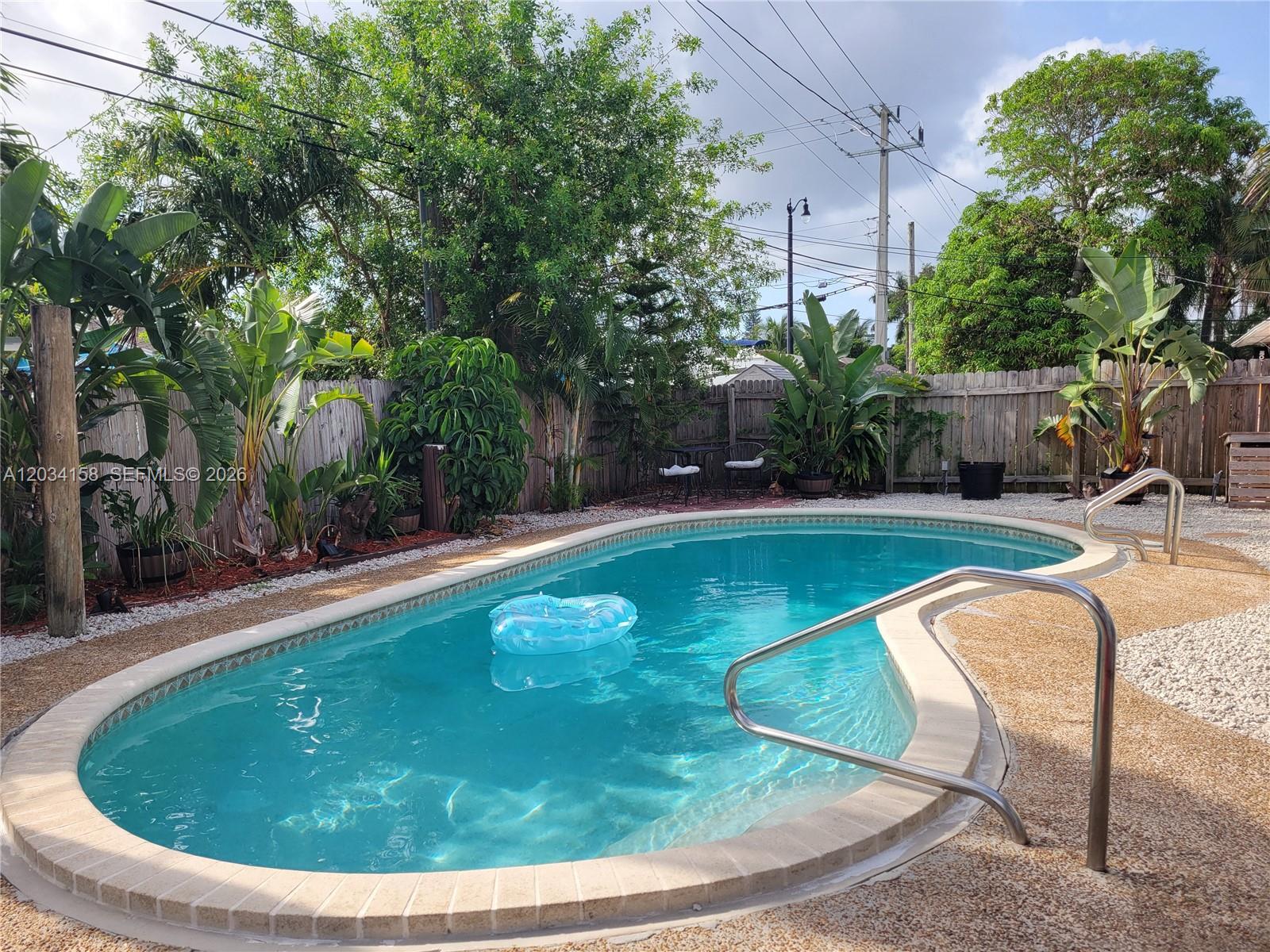 An oval swimming pool with a blue float sits in a backyard with tropical landscaping — 2560 NE 8th Ter, Pompano Beach FL 33064, POMPANO BEACH, FL