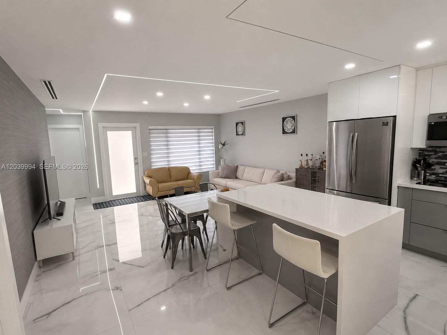 An open-concept living and dining area features white marble floors, a kitchen island, and modern lighting — 7521 Shalimar St, Miramar FL 33023, MIRAMAR, FL