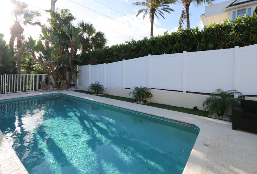 A swimming pool sits in a backyard with a white privacy fence and palm trees — 400 Seaside Lane, Juno Beach FL 33408, JUNO BEACH, FL
