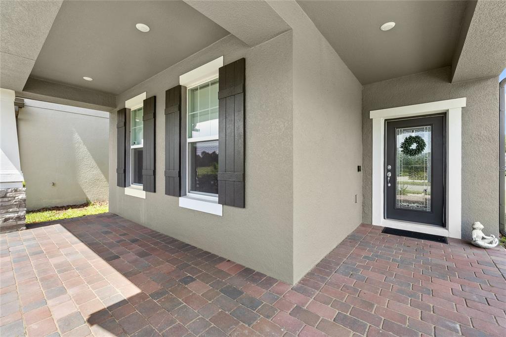A covered front porch features brick pavers, a dark front door, and a window with shutters — 13155 SPRING GROVE WAY, WINTER GARDEN, FL