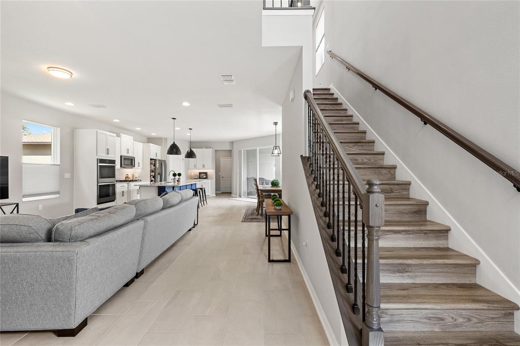 An open-concept living area features a gray sectional sofa, kitchen, and a wooden staircase — 13155 SPRING GROVE WAY, WINTER GARDEN, FL