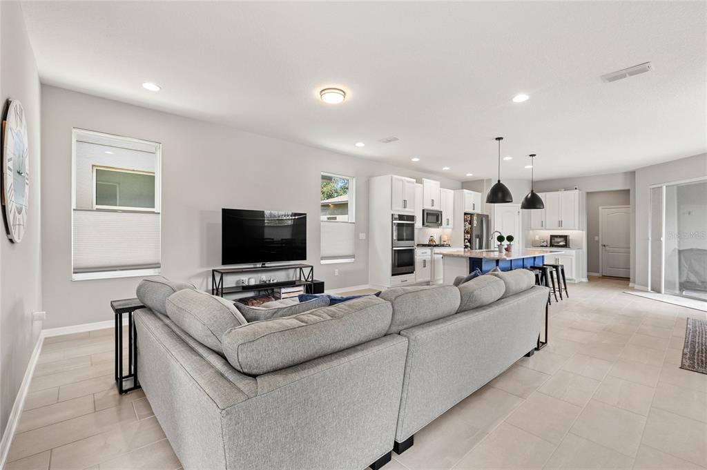 A bright open-concept living room features a large gray sectional sofa facing a television — 13155 SPRING GROVE WAY, WINTER GARDEN, FL