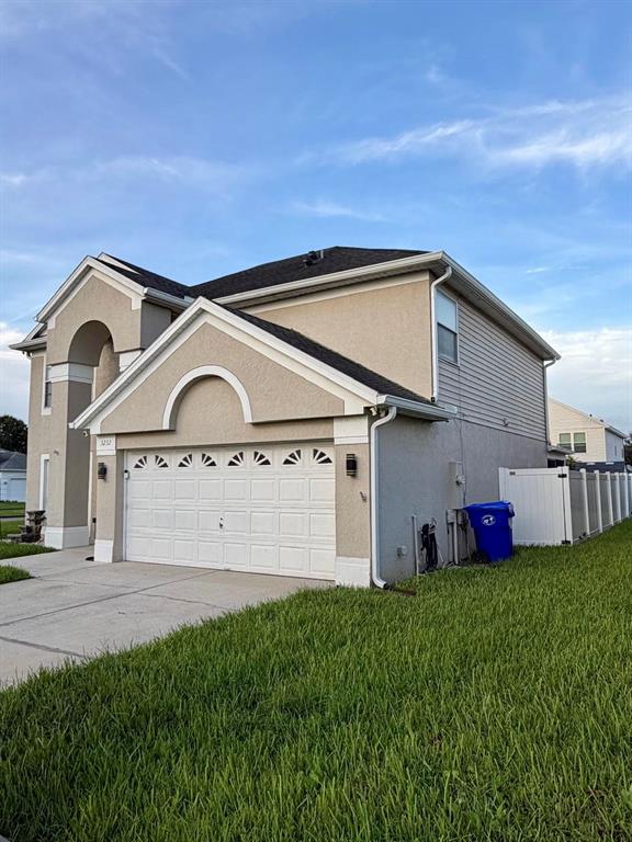 A two-story house with a beige stucco exterior, a white garage door, and a blue bin — 3232 HERONS POINT CIRCLE, KISSIMMEE, FL
