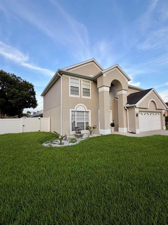 A two-story beige house with a white garage and a white fence in the yard — 3232 HERONS POINT CIRCLE, KISSIMMEE, FL