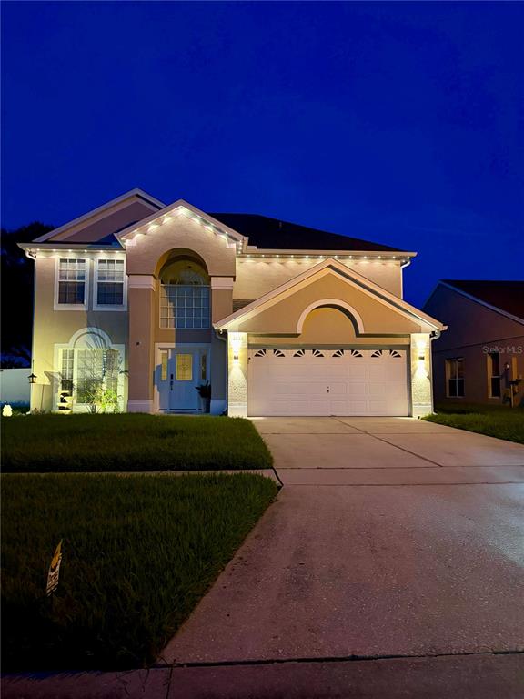 A two-story house with a beige exterior, a two-car garage, and exterior accent lighting — 3232 HERONS POINT CIRCLE, KISSIMMEE, FL