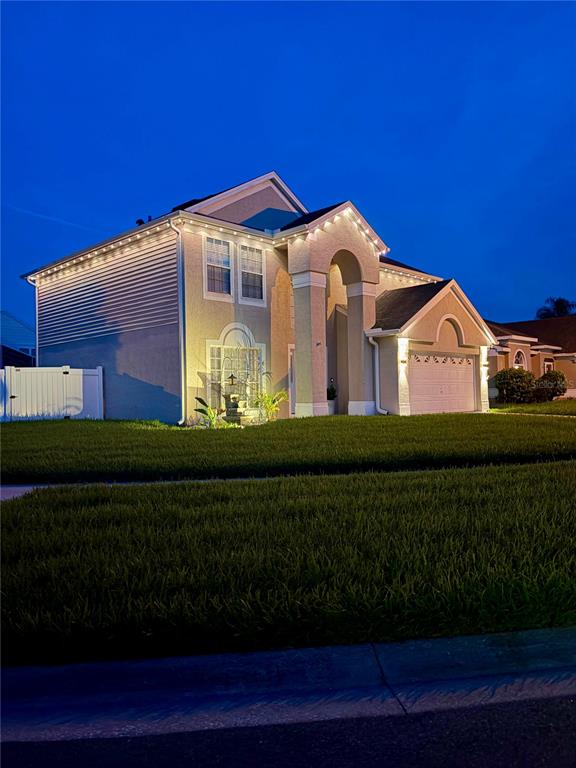 A two-story suburban house with a tan stucco exterior and illuminated roofline at dusk — 3232 HERONS POINT CIRCLE, KISSIMMEE, FL