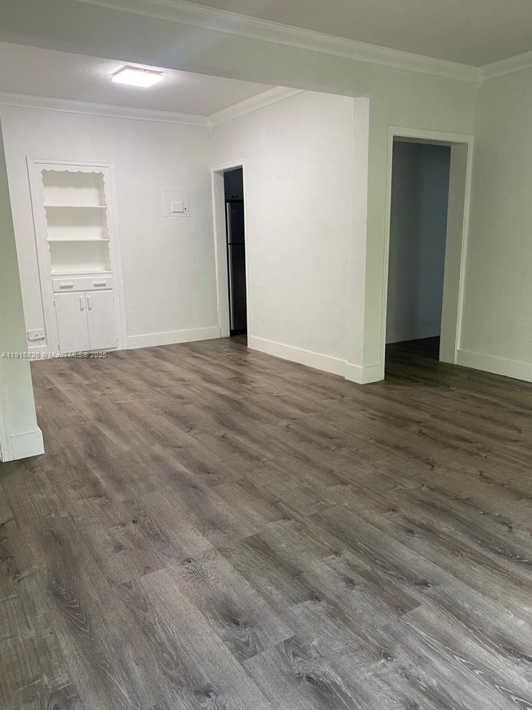 An empty room features wood-look laminate flooring, white walls, and a built-in white cabinet — 6805 Abbott Ave # 7, Miami Beach FL 33141, MIAMI BEACH, FL