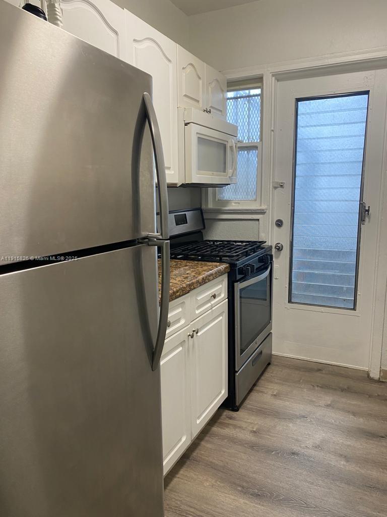 A kitchen features white cabinets, stainless steel appliances, granite countertops, and a glass-paneled door — 6805 Abbott Ave # 7, Miami Beach FL 33141, MIAMI BEACH, FL