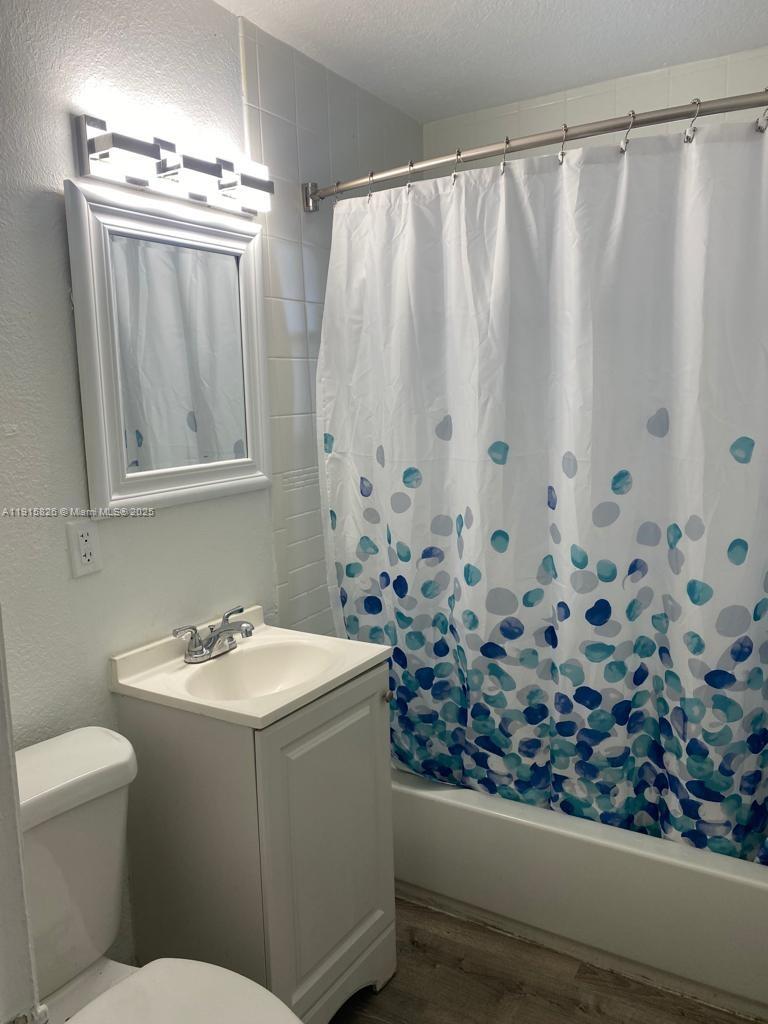 A bathroom features a white vanity, a mirror, a light fixture, and a patterned shower curtain — 6805 Abbott Ave # 7, Miami Beach FL 33141, MIAMI BEACH, FL