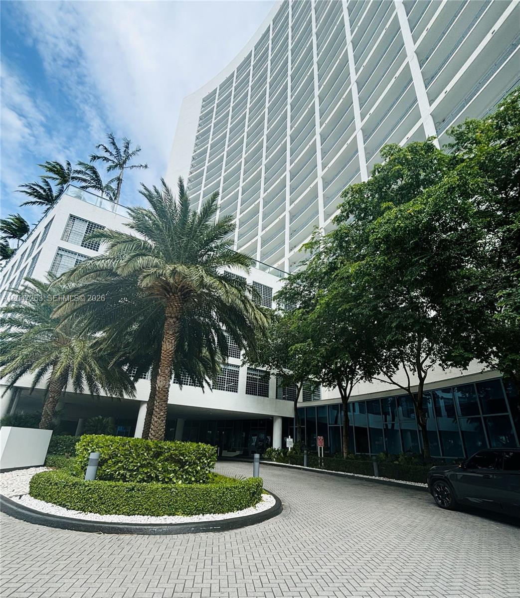 A modern high-rise building features a curved facade, a circular driveway, and lush landscaping — 601 NE 36th St # 2203, Miami FL 33137, MIAMI, FL