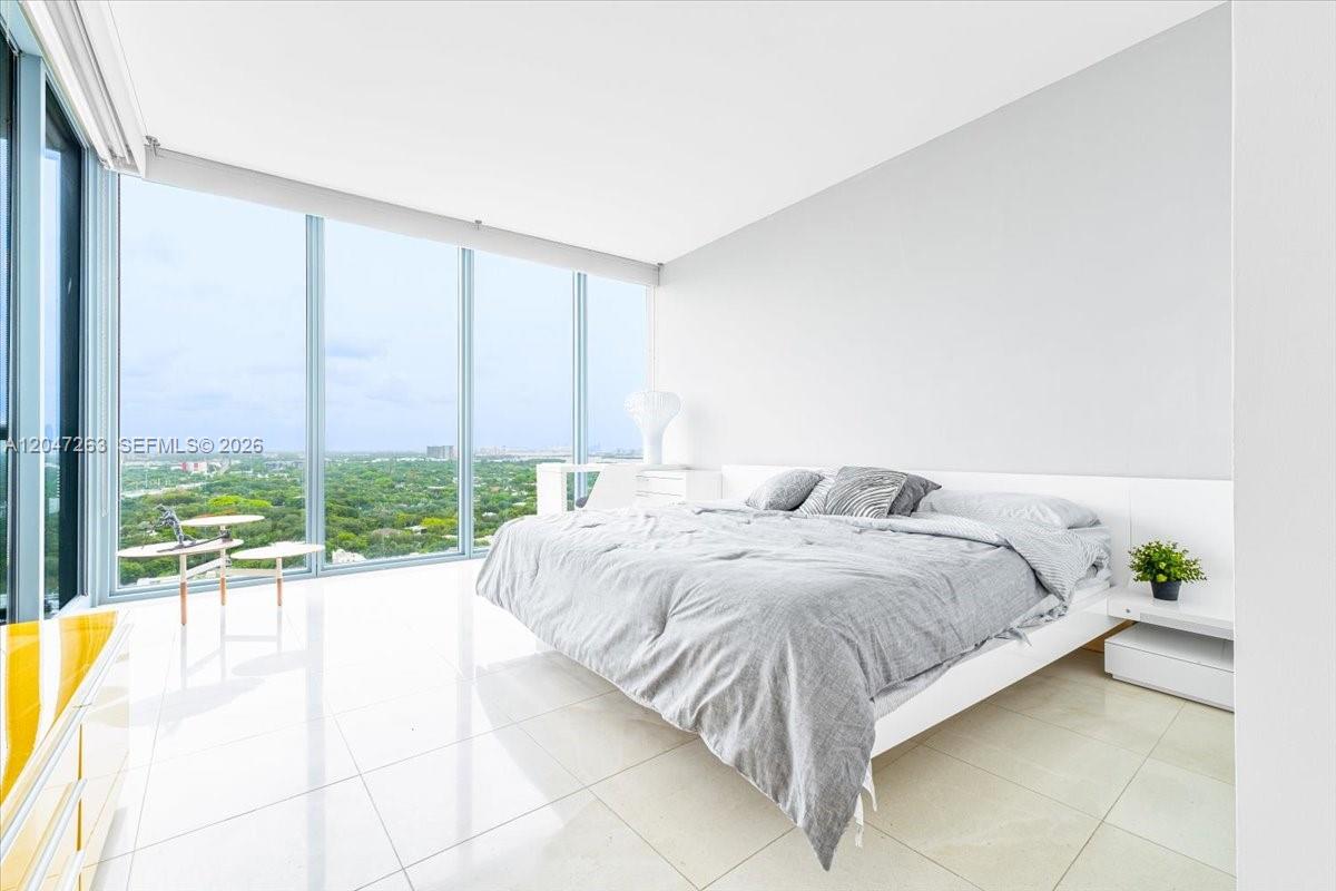 A modern bedroom features a white bed, glossy tile floors, and floor-to-ceiling windows — 601 NE 36th St # 2203, Miami FL 33137, MIAMI, FL