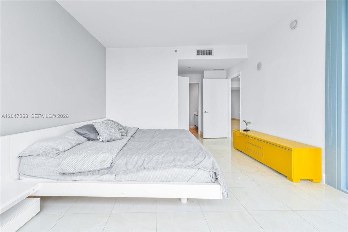 A bedroom features a white bed, a bright yellow console table, and white tile flooring — 601 NE 36th St # 2203, Miami FL 33137, MIAMI, FL