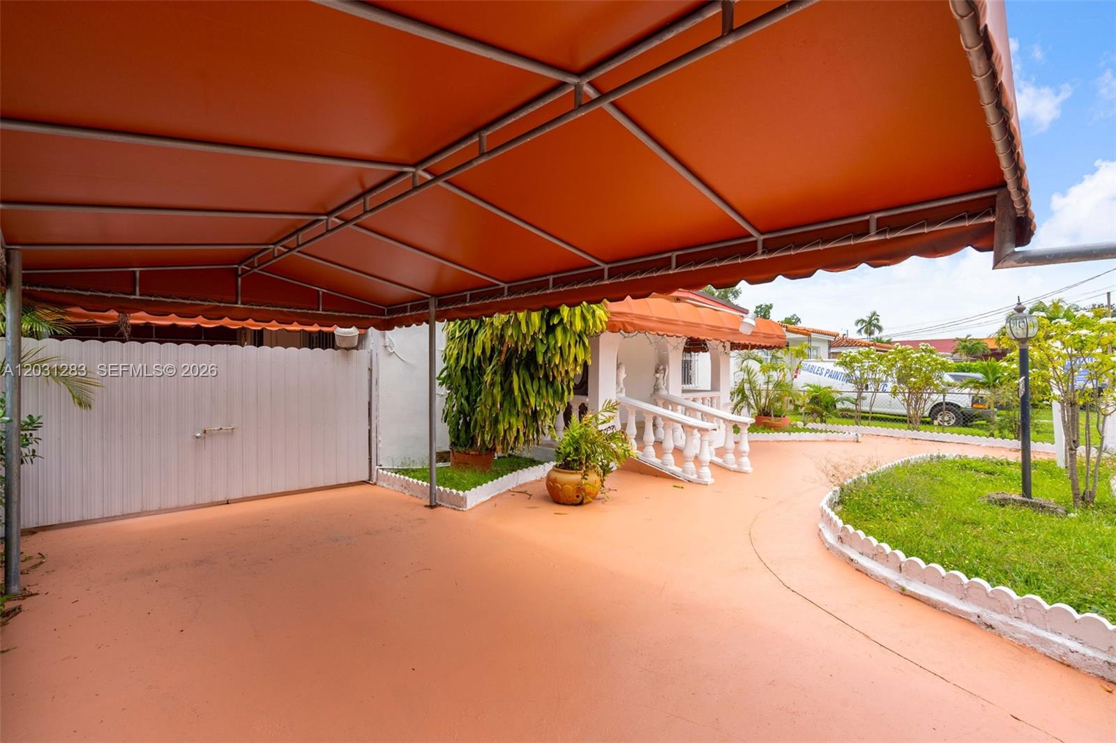 A paved driveway features a large orange metal awning and a white picket fence — 615 SW 62nd Ct, Miami FL 33144, MIAMI, FL