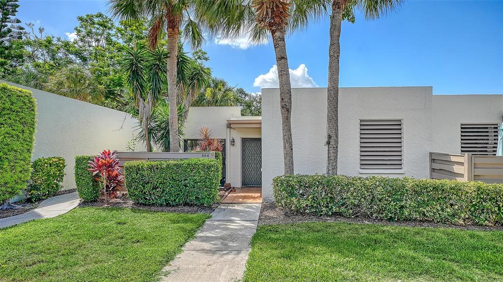 A single-story residential building with a concrete walkway, palm trees, and manicured hedges — 664 WOODLAWN DRIVE, BRADENTON, FL
