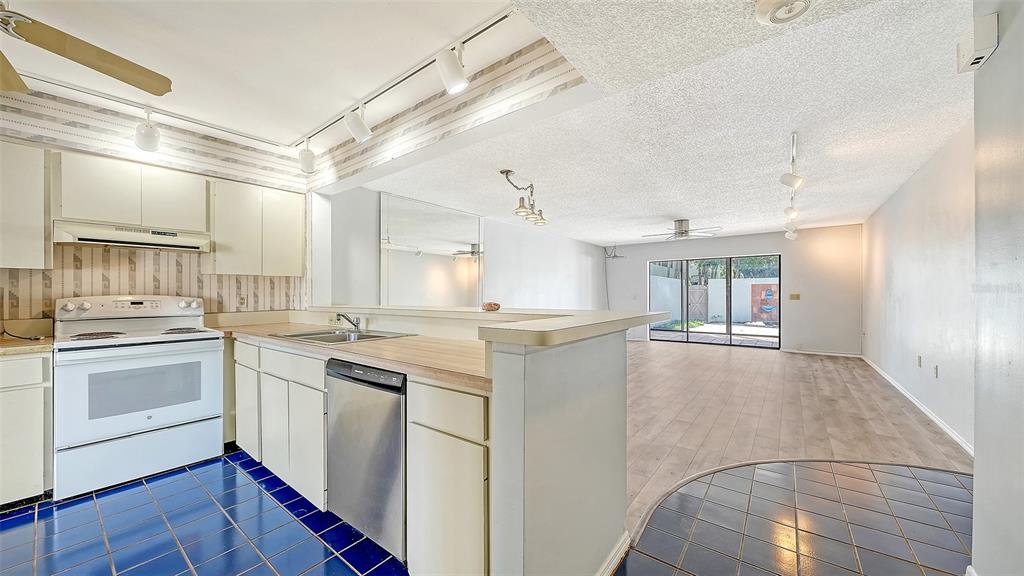 A kitchen with blue tile floors and white cabinets overlooks a living area with wood-look flooring — 664 WOODLAWN DRIVE, BRADENTON, FL