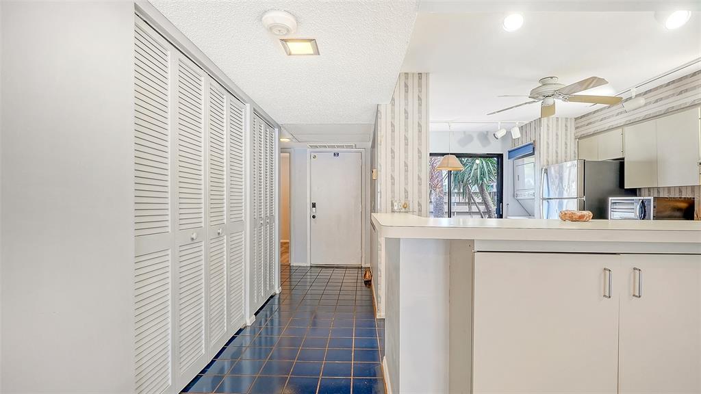 A hallway with blue tile flooring leads to a white door past a kitchen counter — 664 WOODLAWN DRIVE, BRADENTON, FL