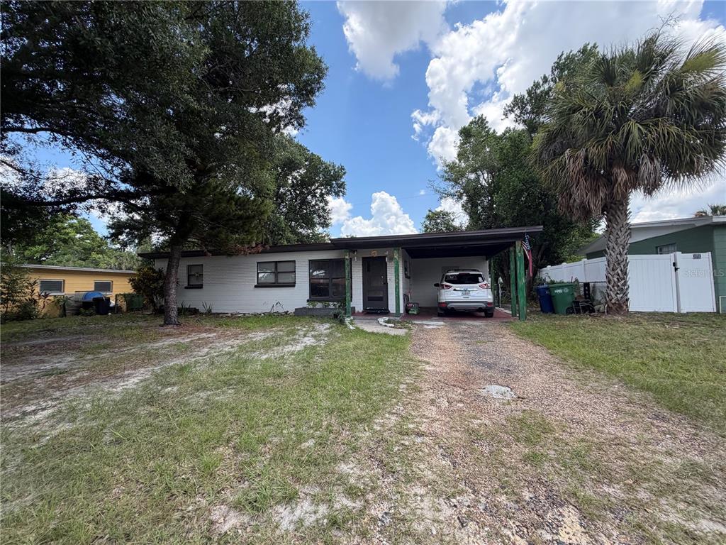 A single-story white house with a carport and a gravel driveway under a blue sky — 10111 N OLA AVENUE, TAMPA, FL