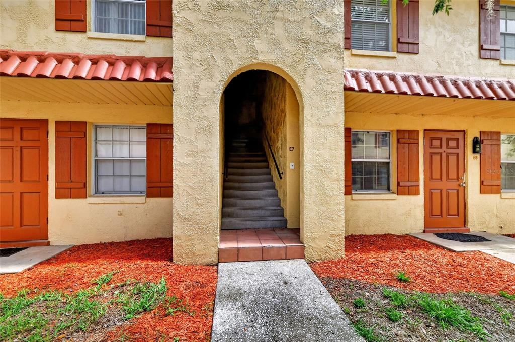 The exterior of a two-story apartment building features stucco walls, red shutters, and a central staircase — 1112 W MAIN STREET UNIT E7, LEESBURG, FL