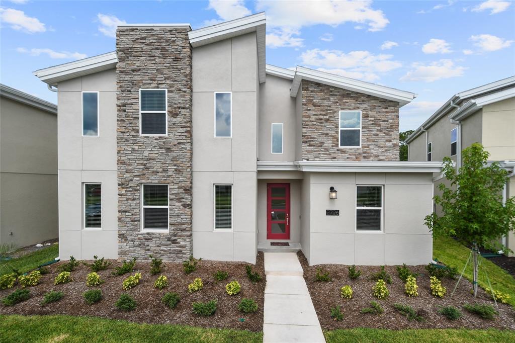 A two-story house features a stone facade, light-colored stucco, and a bright red front door — 2726 OXYMORON WAY, KISSIMMEE, FL