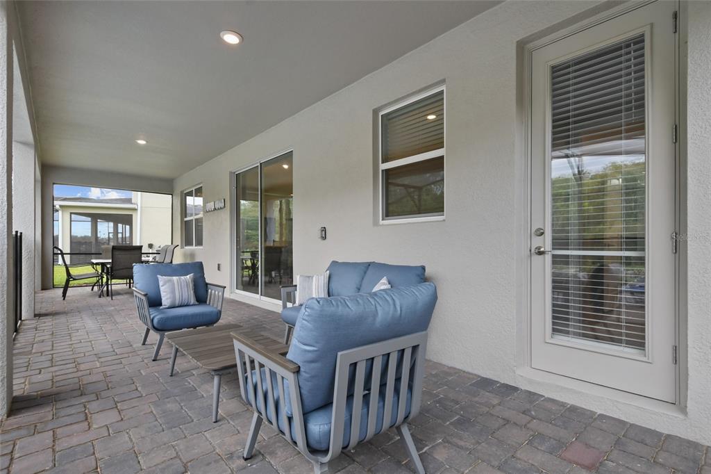 A covered patio features paver flooring, blue outdoor furniture, and a glass-paned door — 2726 OXYMORON WAY, KISSIMMEE, FL
