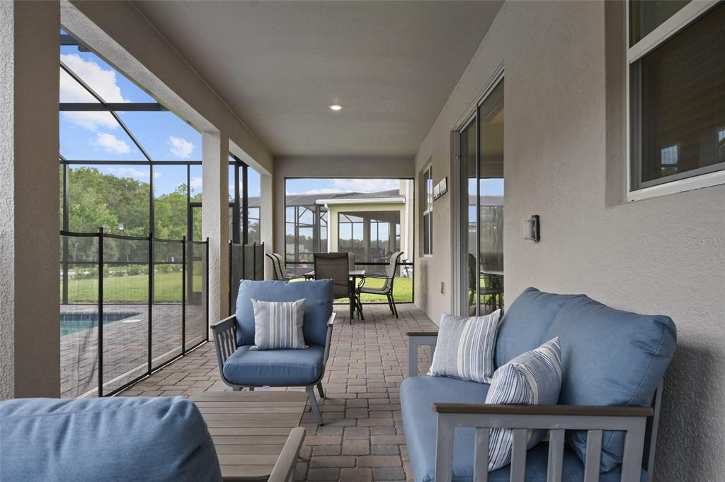 A covered patio features blue outdoor furniture, brick pavers, and a screened-in pool area — 2726 OXYMORON WAY, KISSIMMEE, FL