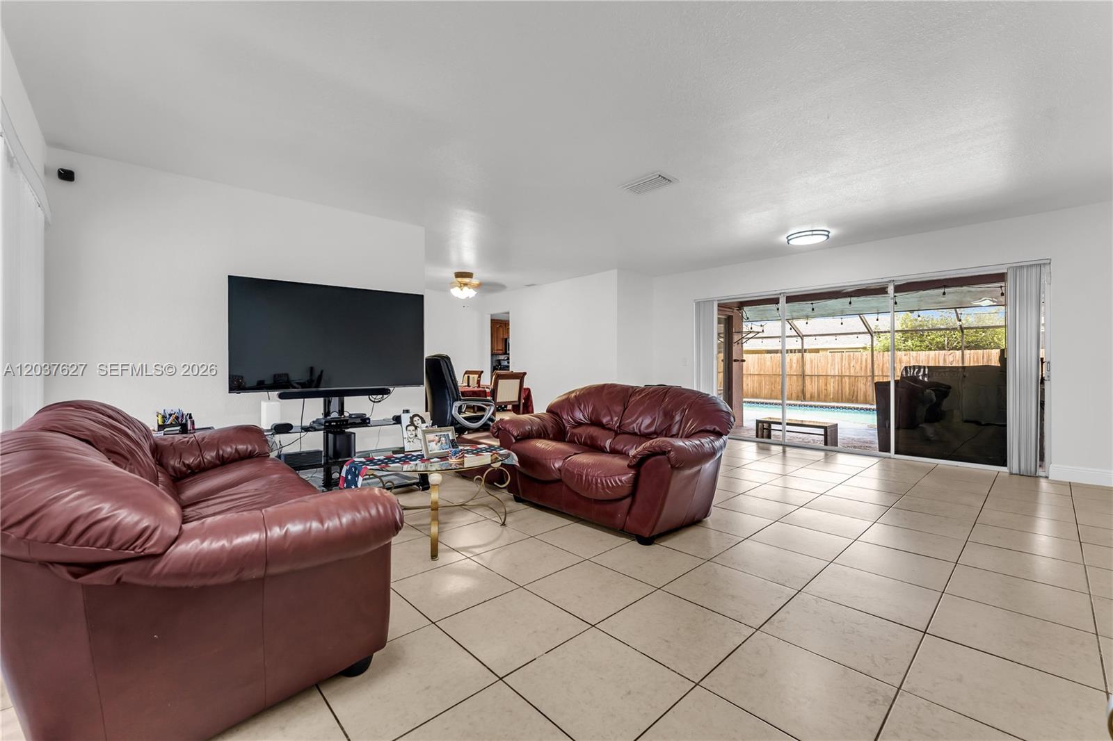 A living room features tile flooring, two leather sofas, a television, and sliding glass doors — 2751 NW 107th Ter, Sunrise FL 33322, SUNRISE, FL
