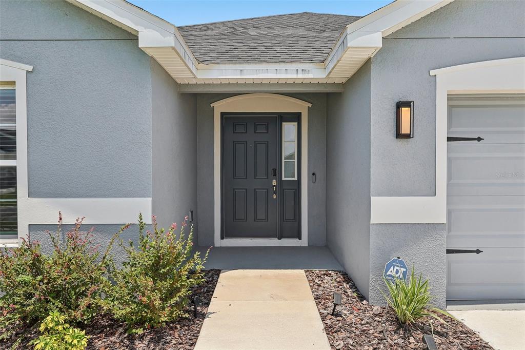 The front entrance of a house features a dark door, a concrete walkway, and landscaping — 797 CYPRESS CREEK RUN, ST CLOUD, FL