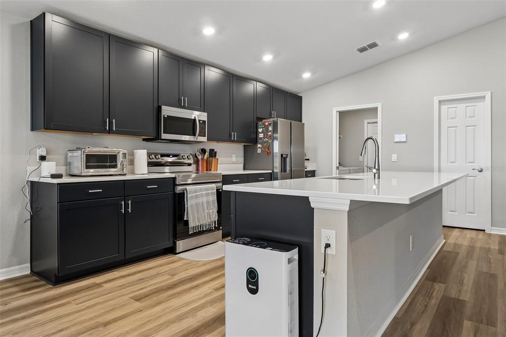A kitchen features dark cabinets, stainless steel appliances, a white island, and light wood flooring — 797 CYPRESS CREEK RUN, ST CLOUD, FL