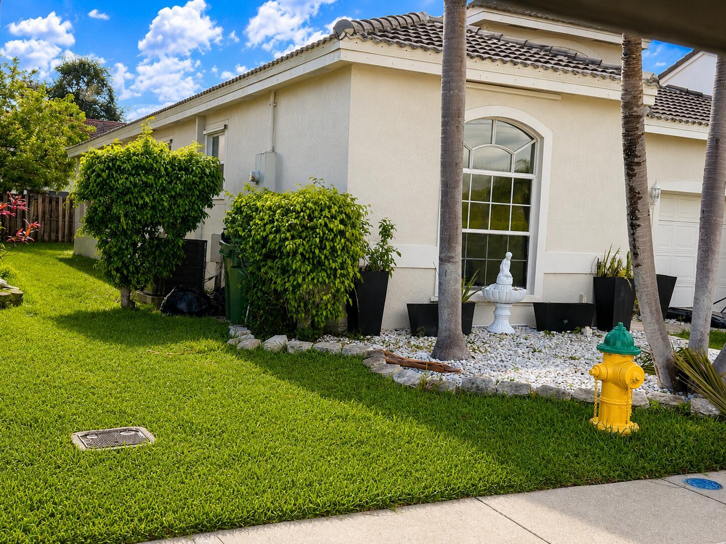 A yellow fire hydrant sits on a grassy lawn in front of a beige stucco house — 3071 Dogwood Lane, Margate FL 33063, MARGATE, FL