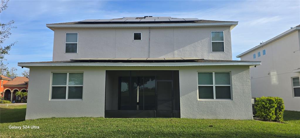 The rear exterior of a two-story house features a screened-in patio and rooftop solar panels — 18410 BLUE HERON CIRCLE, DEER ISLAND, FL