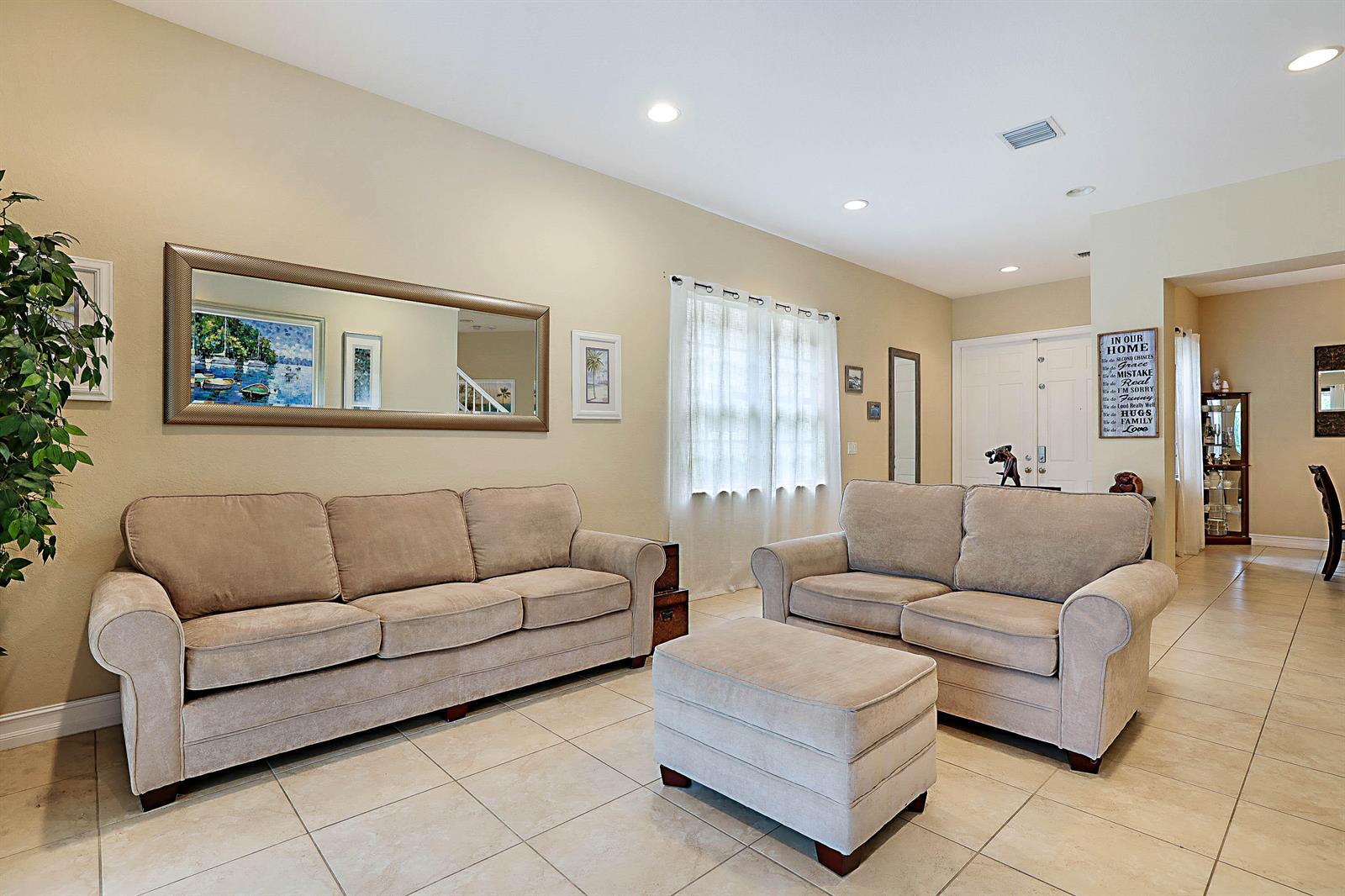 A living room features two beige sofas, a matching ottoman, and tile flooring — 7593 NW 113th Avenue, Parkland FL 33076, PARKLAND, FL