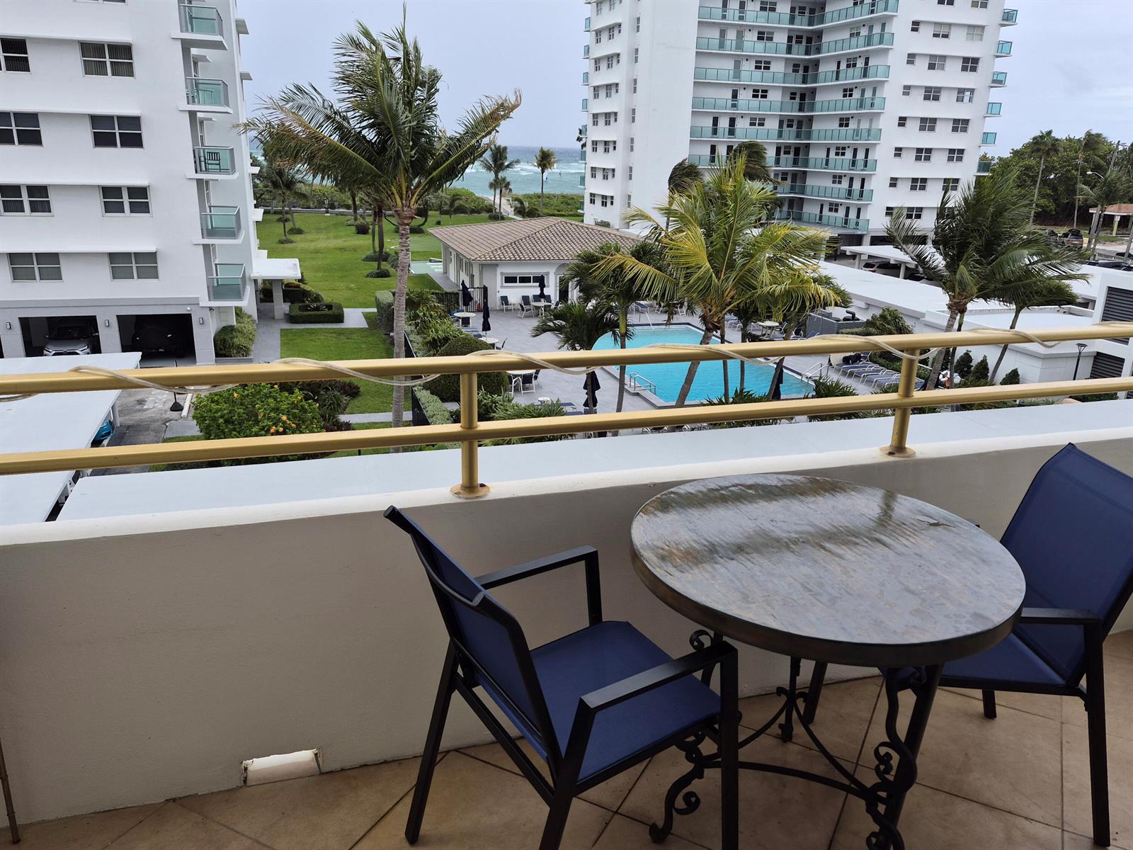 A balcony features a round table and two chairs overlooking a pool and the ocean — 1630 N Ocean Boulevard # 314, Pompano Beach FL 33062, POMPANO BEACH, FL
