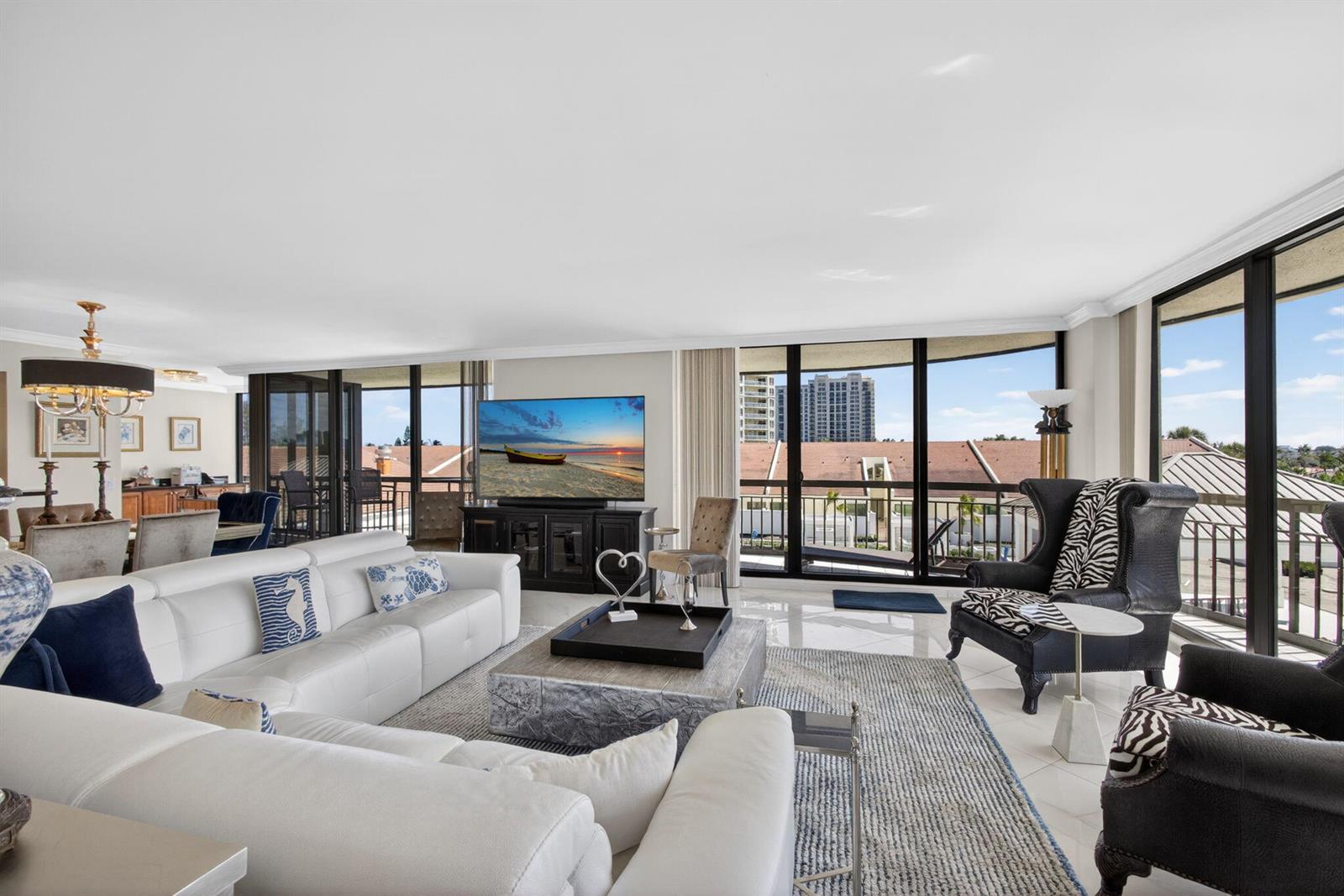 A bright living room features a white sectional, patterned armchairs, and floor-to-ceiling windows — 4100 N Ocean Drive # 304, Riviera Beach FL 33404, RIVIERA BEACH, FL