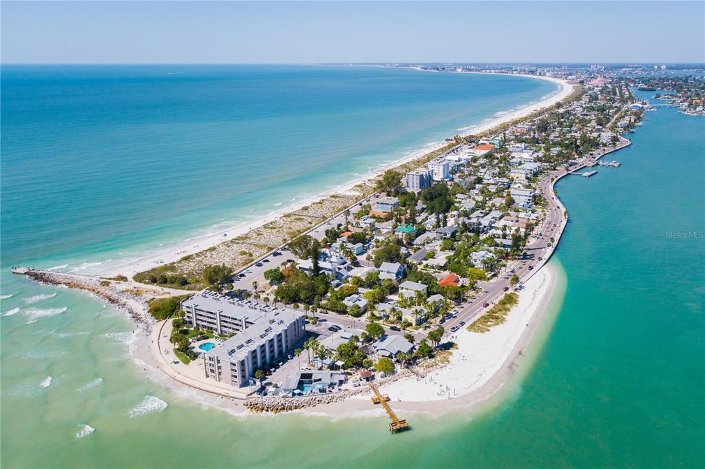 Aerial view of a coastal barrier island featuring beachfront buildings, residential homes, and sandy shores — 15TH AVENUE, ST PETE BEACH, FL
