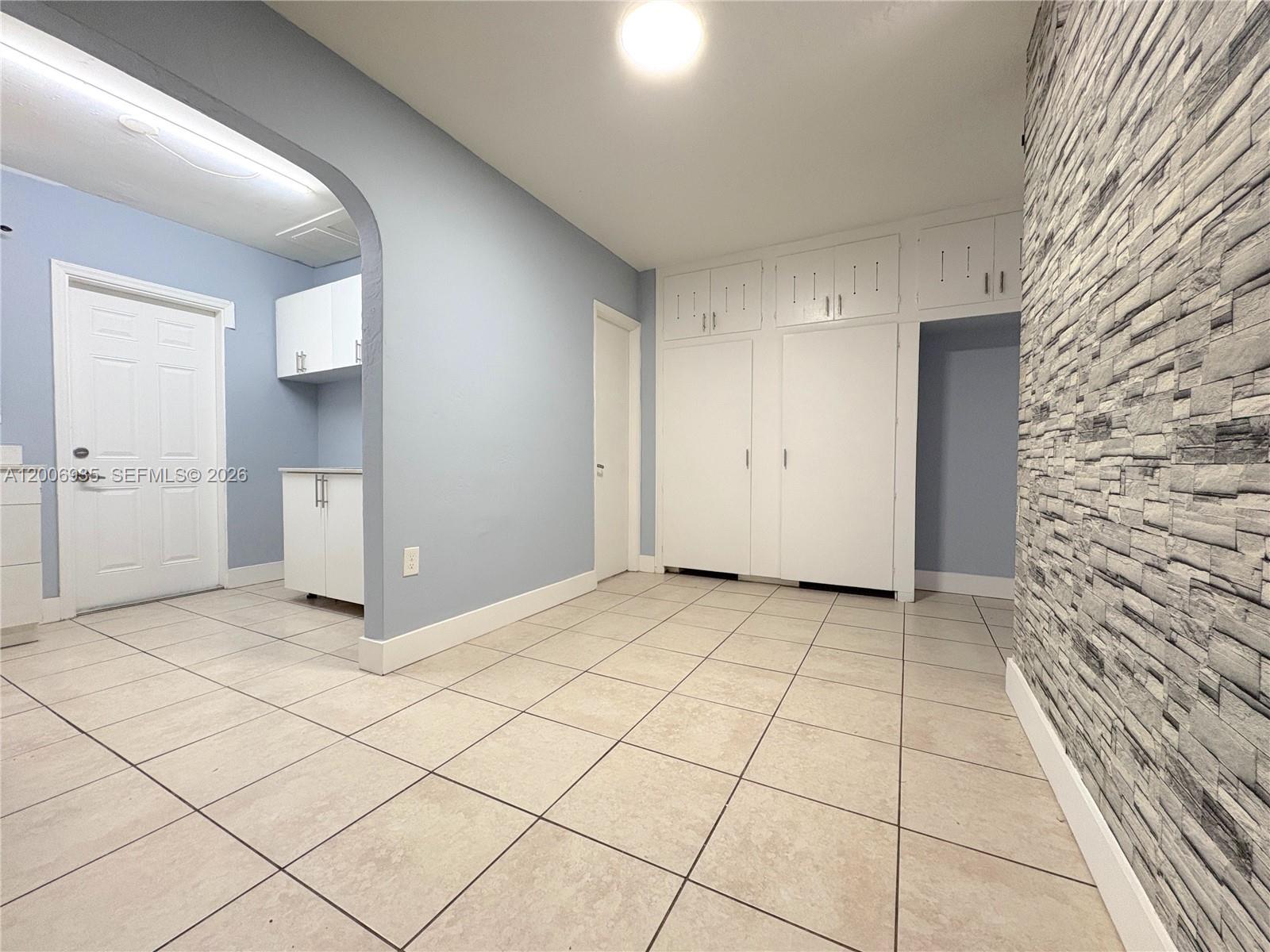 A room with light blue walls, tile flooring, white cabinetry, and a stone-textured accent wall — 1815 Mckinley St # 9, Hollywood FL 33020, HOLLYWOOD, FL